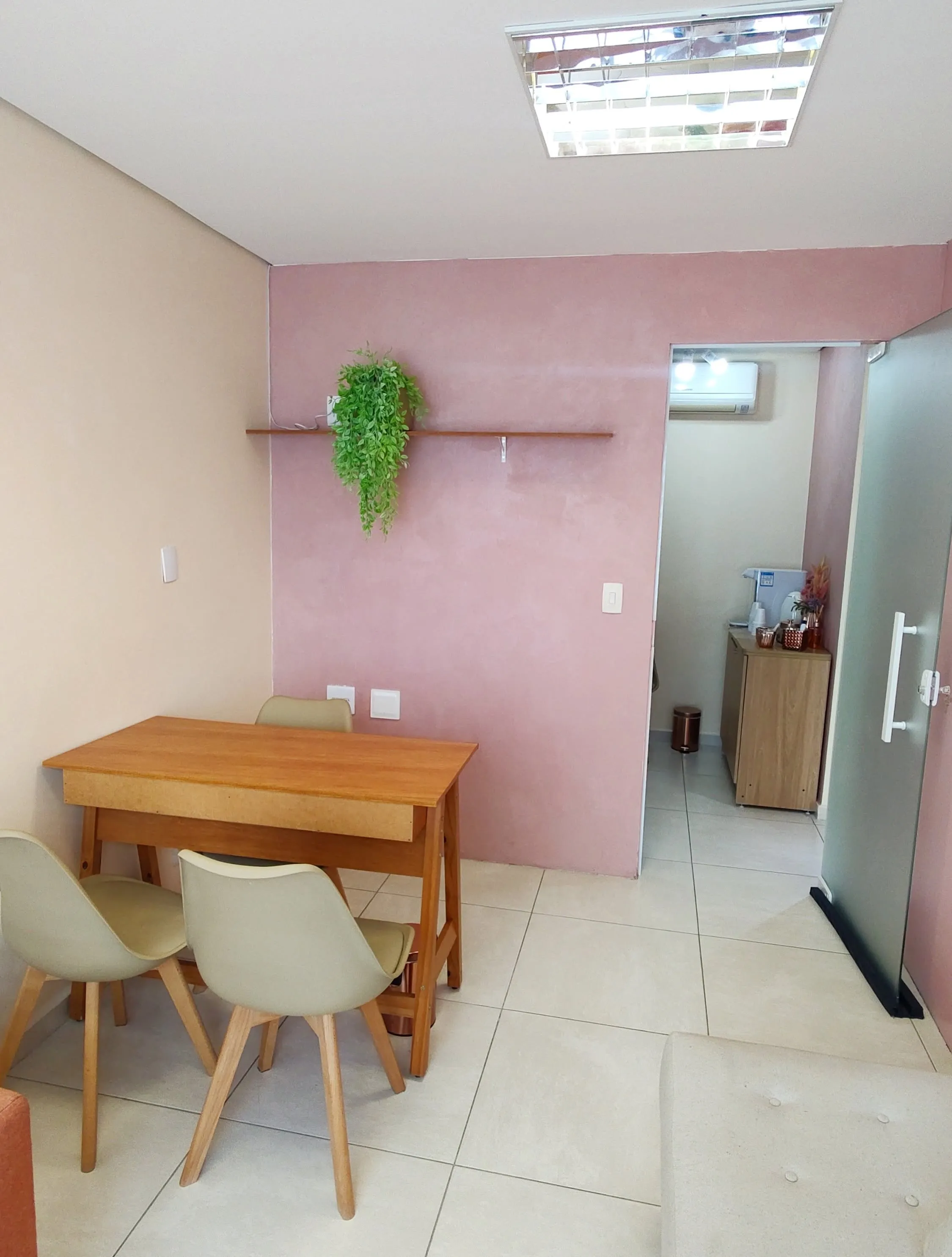 Mesa com três cadeiras na Sala Rosa, com parede rosa e prateleira com planta