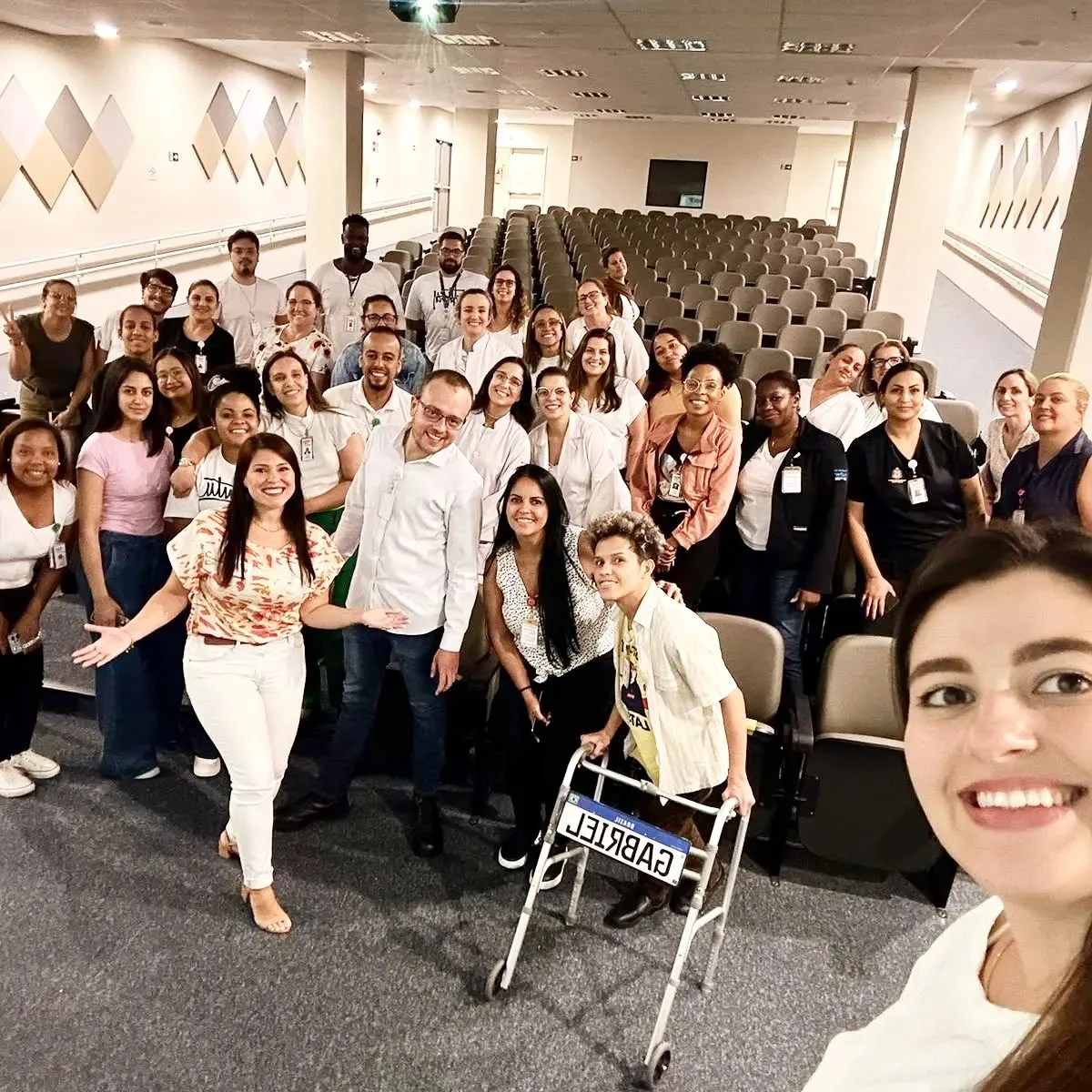 Karen Buratti com um grande grupo de profissionais de saúde em um auditório após a palestra