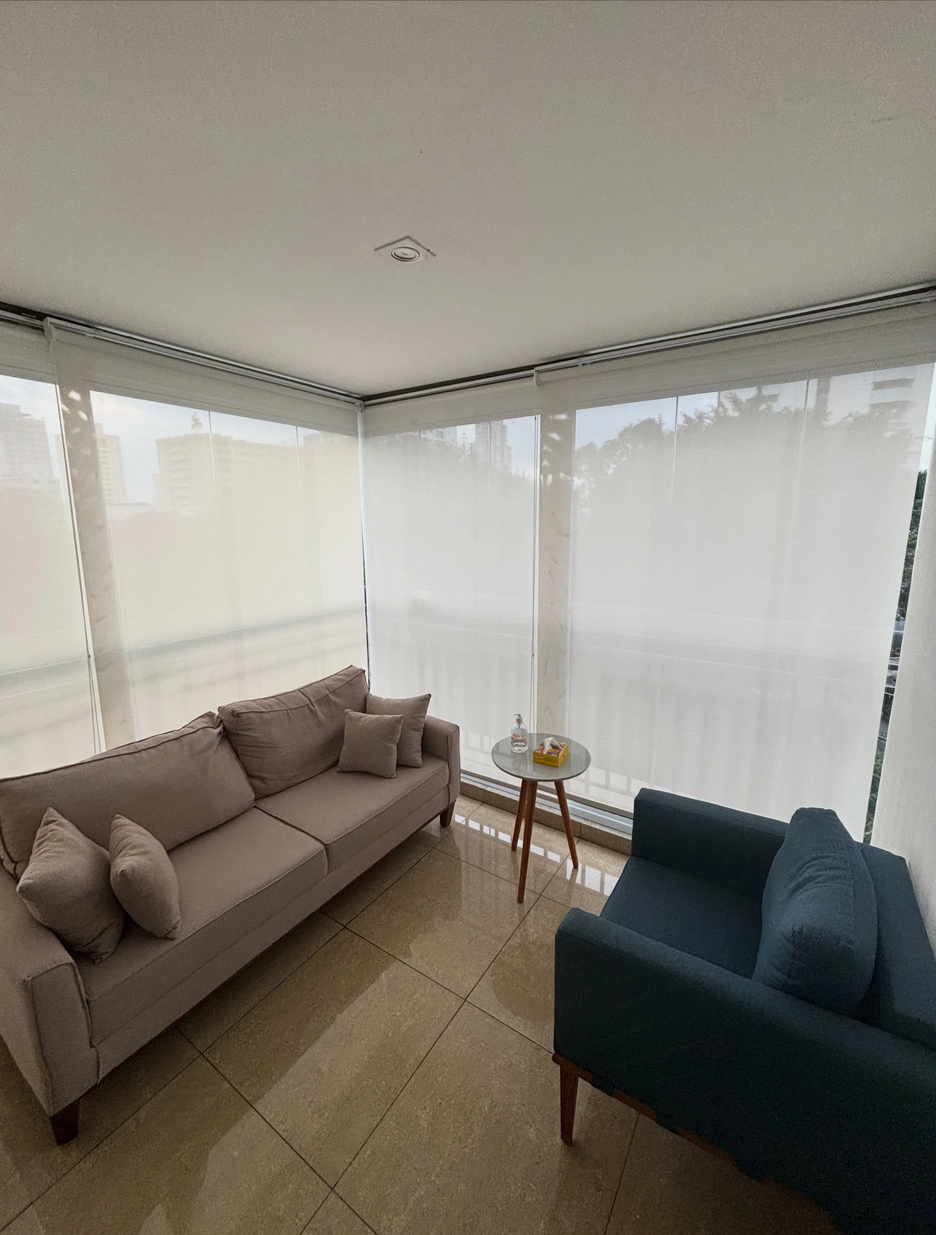 Sacada da Sala Azul com sofá, poltrona azul e cortinas translúcidas